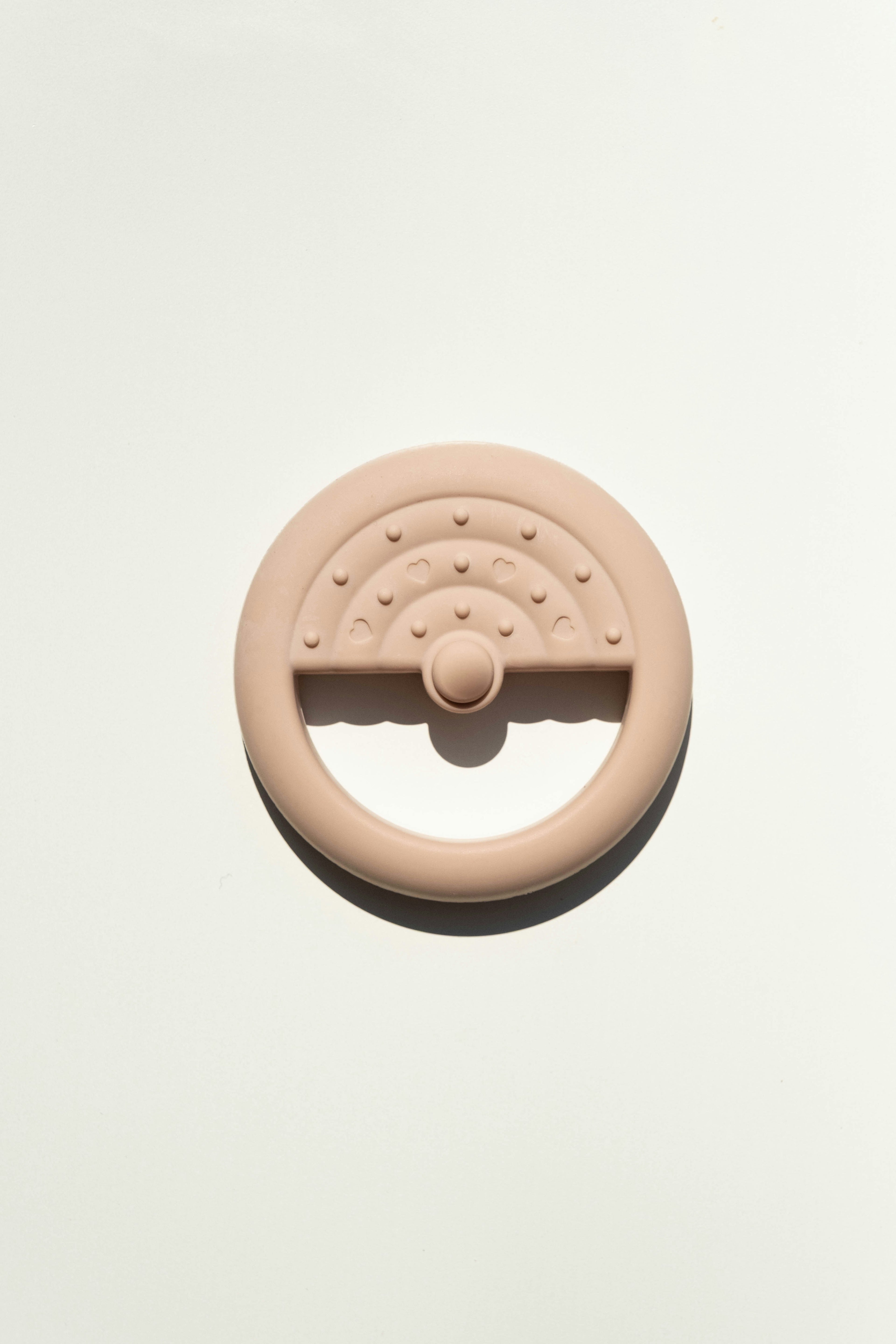 Pale blush silicone teether shaped like a steering wheel