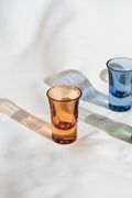 Hand-blown coloured glass tumblers on linen with afternoon light