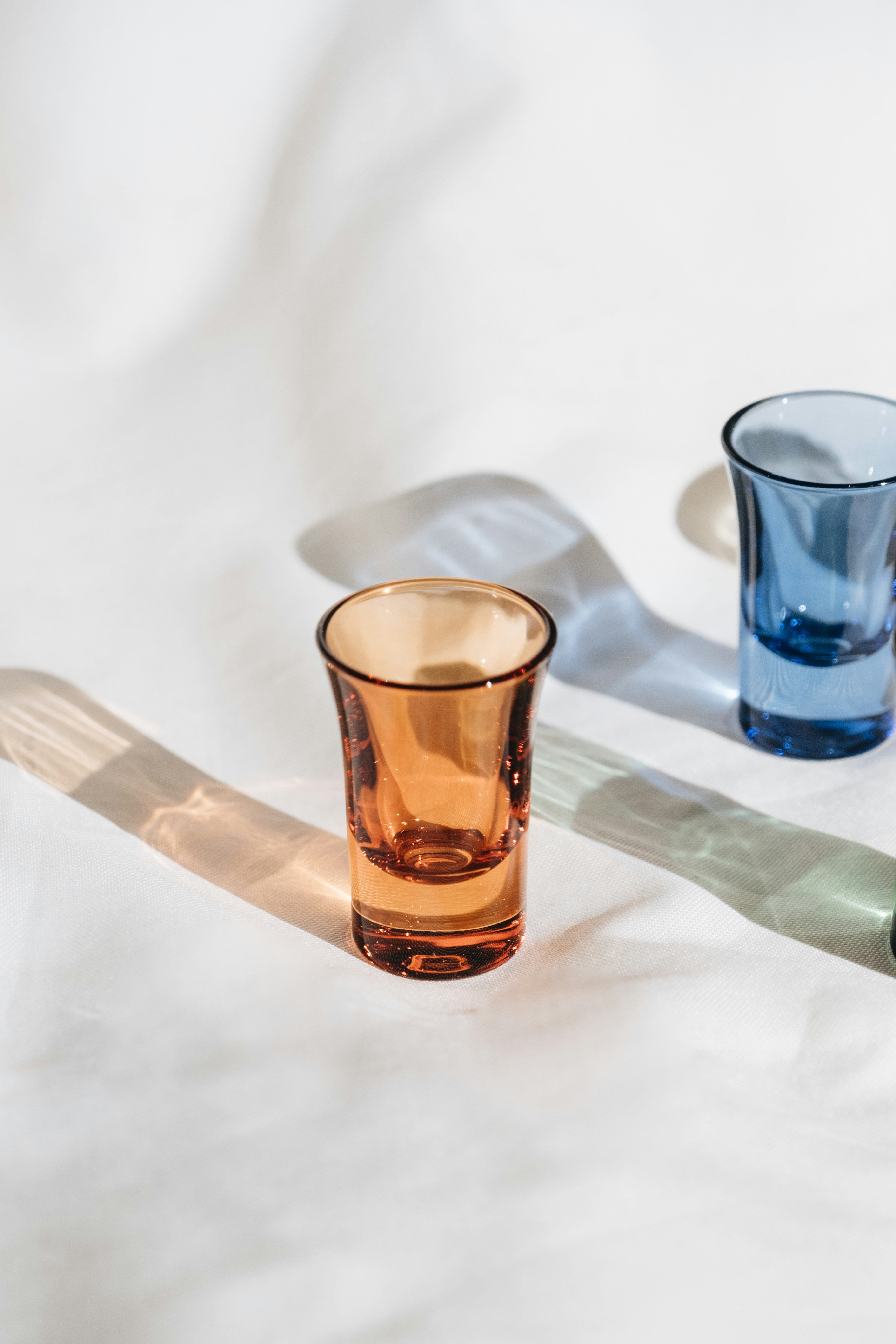 Hand-blown coloured glass tumblers on linen with afternoon light