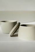 Pair of matte cream stoneware mugs with hand-fitted lids