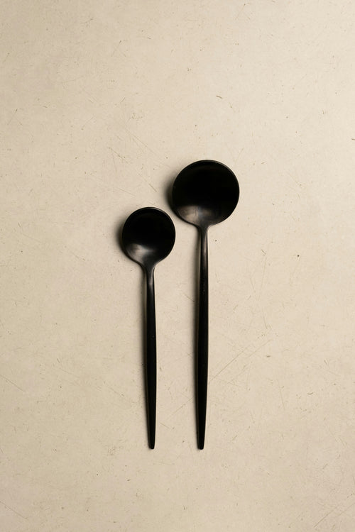 Pair of matte black serving spoons on parchment background